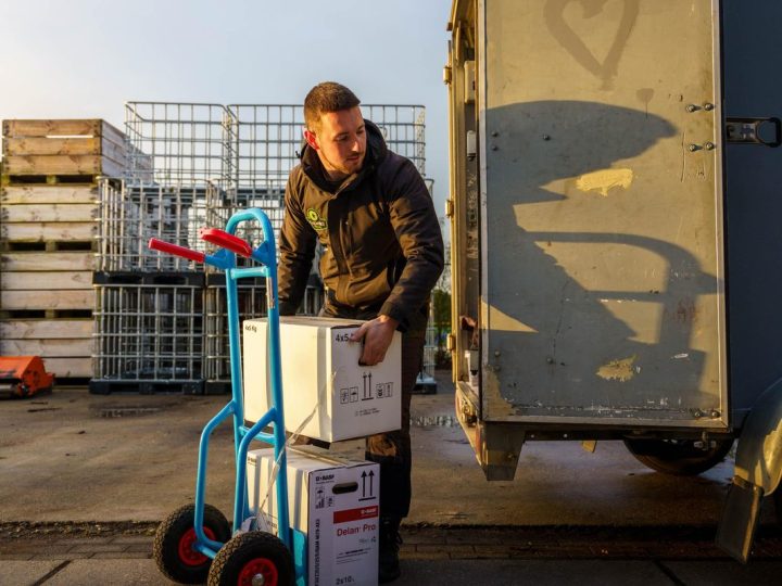 Sam laadt dozen op een steekwagen bij een bedrijfspand